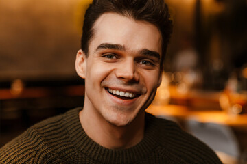 Young white man wearing sweater smiling and looking at camera in cafe