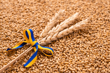 Wall Mural - Bundle of wheat spikes with yellow and blue ribbon in colors of Ukrainian flag on grain pile as background. Concept of food supply crisis and global food scarcity because of war in Ukraine