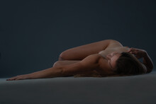 Studio Photo Of A Young Naked Woman Lying Down On The Floor And Touching Herself