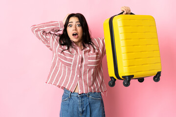 Wall Mural - Young caucasian woman isolated on pink background in vacation with travel suitcase and surprised