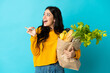 © luismolinero - Young woman holding a grocery shopping bag isolated on blue background intending to realizes the solution while lifting a finger up