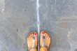 Feet in open sandals with red nail polish on toes on the asphalt background