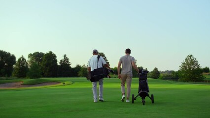 Wall Mural - Rich golf players walking on field. Two active sportsmen carry equipment clubs.