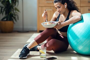 Wall Mural - Sporty young woman eating healthy while listening to music sitting on the floor at home.