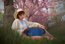 A Young Purple-haired Woman Sitting In A Flowering Orchard Plays A Tongue Drum. It Is A Musical Instrument Similar To Handpan, Hang Or Pantam.