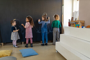 Wall Mural - Group of little girls posing in front of blackboard wall paintings indoors in playroom.