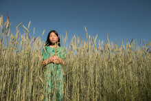 Asian Woman In The Field Of Grain And Wheat In Green Dress Under Blue Sky