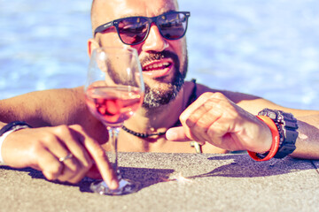 Wall Mural - Portrait of a  happy smiling bearded Man beautiful  holding   a Glass of rose Wine by the swimming pool on the empty deck of a cruise liner.Vacation and travel conceptl