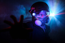 Kid In Protective Respirator With Bright Shining Flashlight Observing Territory With Outstretched Arm While Robbing Dark Mint With Smoke