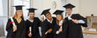 © Studio Romantic - Happy students celebrating graduation. Cheerful mixed race multiethnic male and female university graduates in hats and robes standing in classroom, holding diploma scrolls and smiling at camera