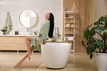 Wall Mural - Beautiful young woman sitting on edge of tub in bathroom