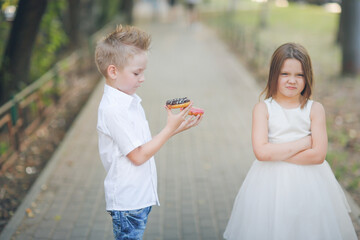 boy child treats harmful offended girl with donuts, asks for forgiveness, wants to make friends. Cute funny romantic couple of kids.