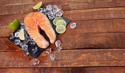 Red fish steak on a wooden brown table with lime slices and ice. Trout steak on a brown background. Healthy food