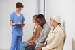 © Mediaphotos - Group of three people sitting in queue waiting for consultation in modern hospital, medical worker standing near them making notes