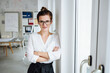 © contrastwerkstatt - young woman with glasses stands in office and looks into camera