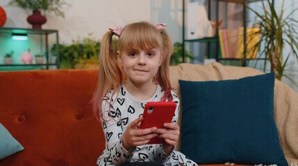 Wall Mural - Wow. Excited amazed kid girl use mobile cell phone say wow yes raising hands in surprise looking at camera with big eyes, shocked by sudden victory. Happy winner child toddler celebrate alone at home