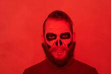 Portrait Of Angry Bearded Zombie Man With Gloomy Makeup Standing In Red Light, Halloween Concept