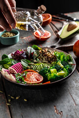 hands holding oil. vegetable vegetarian buddha bowl avocado, blood orange, broccoli, watermelon radish, spinach, quinoa, pumpkin seeds. vertical image, place for text