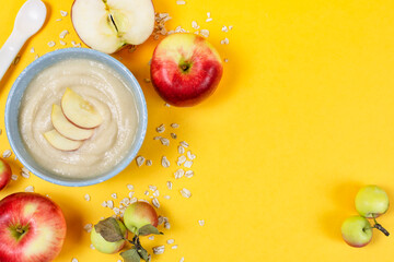 Wall Mural - Oatmeal porridge for the baby from ground cereals in a blue bowl, red ripe apples on a yellow background. Place for text, recipe. The first complementary feeding of the child.