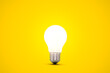 Glowing light bulb isolated on a bright yellow background.