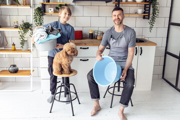 Wall Mural - Handsome father and his teenager son spending quality time together, having fun. Men doing chores, cleaning, sorting laundry in the kitchen at home. Pet dog near them