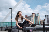 A young girl works at a laptop sitting on a bench, against the backdrop of the Gateshead Millennium Bridge. The freelancer works outdoors. The concept of a free office. North East England