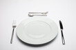 Empty white plate with spoon, knife and fork on white background