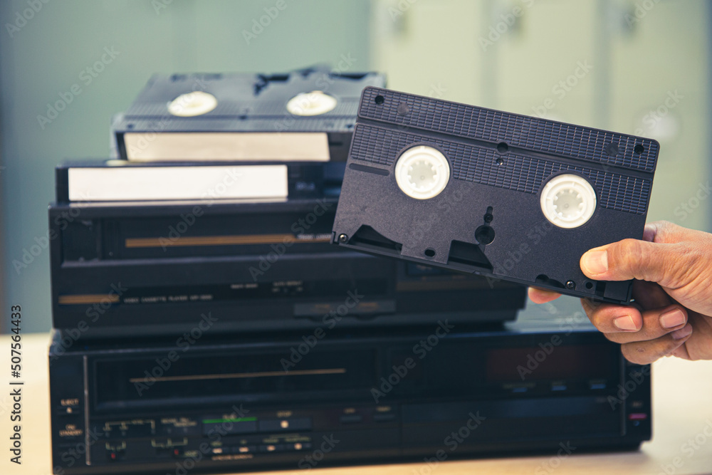 Close-up hand chooses video cassette tape VHS old retro style on video record playback concept of vintage electric and electronic appliances multimedia player device old fashioned.