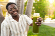 Young black man showing glass bottle of green juice to camera. Focus on man face.