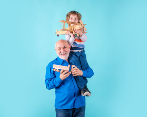 Grandfather and grandson piggyback with toy plane and wooden truck. Men generation granddad and grandchild.