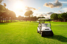 Golf Cart In Fairway Of Golf Course With Green Grass Field With Cloudy Sky And Trees At Sunset