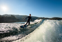 Man Wakesurfer Skillfully Balancing On The Splashing Wave On Blue Sky Background