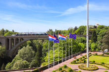 View Of The Adolphe Bridge In Luxembourg City. Flags Of Luxembourg And The European Union Fly In The Foreground
