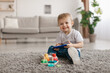© Prostock-studio - Portrait of adorable toddler boy holding smartphone, sitting on floor carpet, looking and smiling at camera, copy space