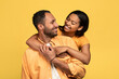 Affectionate young black woman hugging her boyfriend, looking in his eyes on yellow studio background