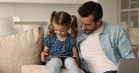 Wall Mural - Addicted to modern technology happy two generations family using different gadgets, relaxing together on comfortable sofa. Smiling young father cuddling small daughter, teaching playing on tablet.