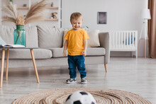 Portrait Of Adorable Toddler Boy Football Fan Playing Soccer Ball And Smiling, Having Fun At Home In Living Room