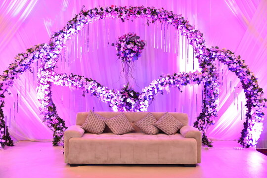 An elegantly staged traditional Malay style wedding with large sofa for the wedding couple to sit and receive blessings from the guests, surrounded by beautiful floral decor and candle light stands..