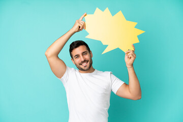 Wall Mural - Young handsome caucasian man isolated on blue background holding an empty speech bubble