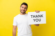 © luismolinero - Young handsome caucasian man isolated on yellow background holding a placard with text THANK YOU with happy expression