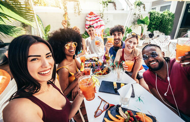 Wall Mural - Multiracial group of friends enjoying meal having backyard dinner party - Young people toasting cocktail glasses together at bar restaurant - Social gathering concept with guys and girls taking selfie