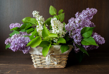 white and purple lilac in wooden basket in front of a dark brown wooden wall