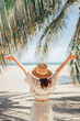 © oatawa - Summer beach vacation concept, Happy woman with hat relaxing at the seaside and looking away, in the summer against a backdrop of palm trees and sea beach.