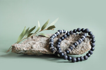 Two bracelets made of natural black volcanic lava stones beads isolated on pastel greenbackground. Handmade jewelry. Woman exoteric accessories. Talismans and amulets. Selective focus