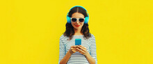 Portrait Of Smiling Young Woman In Headphones Listening To Music With Smartphone On Yellow Background, Blank Copy Space For Advertising Text