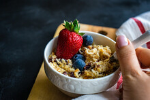Woman Reaching For A Bowl Of Oatmeal With Fresh Blueberries And Strawberry