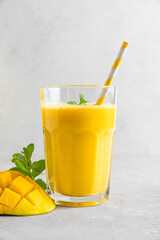 Wall Mural - Fresh yellow mango smoothie in a glass with straw, fresh fruits and mint. Summer tropical drink