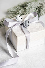 Close-up Of A Gift Box With A Tied Bow And Bell Decoration Next To A Fir Branch