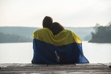 Rear View Of A Couple Sitting On A Jetty Wrapped In A Ukrainian Flag, Thailand