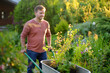 © Maria Sbytova - Handsome gardener man pushing wheelbarrow with plant seedlings in backyard. Spring season work in garden. Person are going to plant trees. Gardening